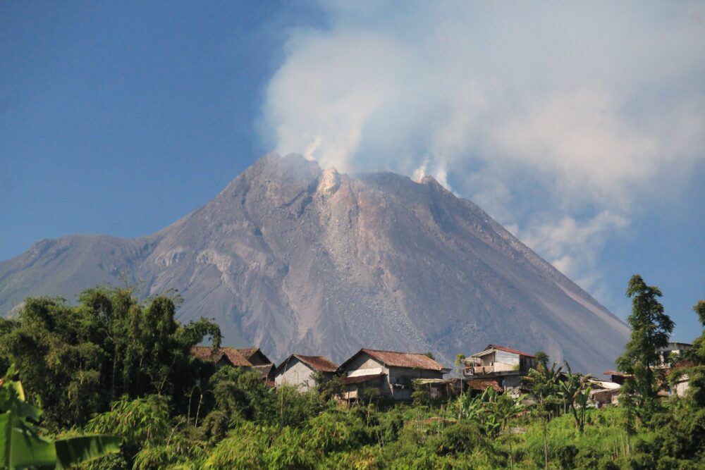 Volcanic ash-covered river valley in Indonesia with muddy lahar flow debris, rural village houses on the banks,...