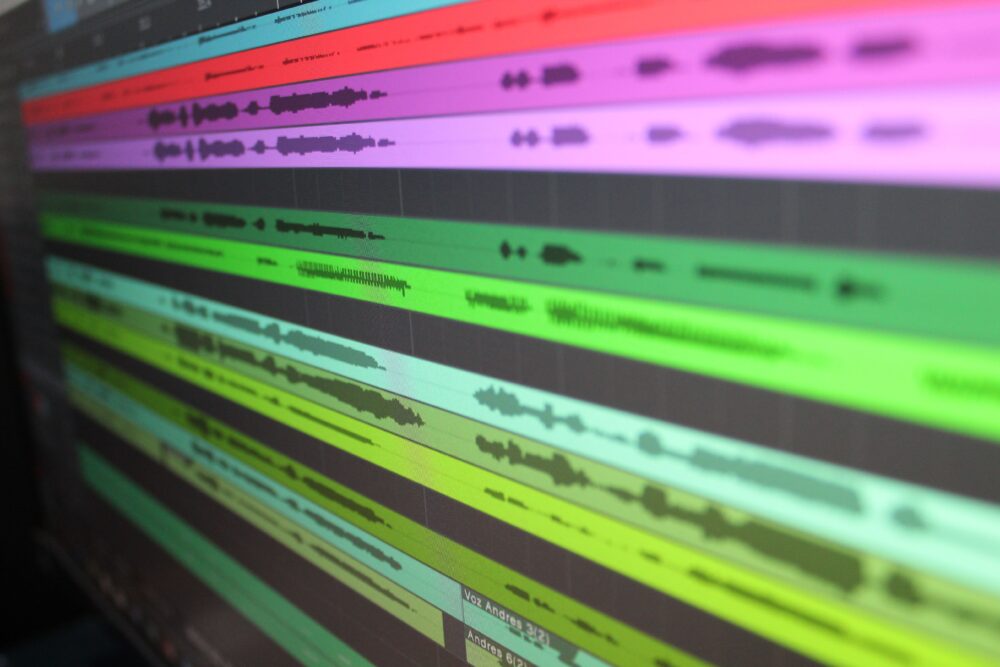 Close-up of audio waveform on a computer screen in a dark music studio, with mixing console blurred in foreground
