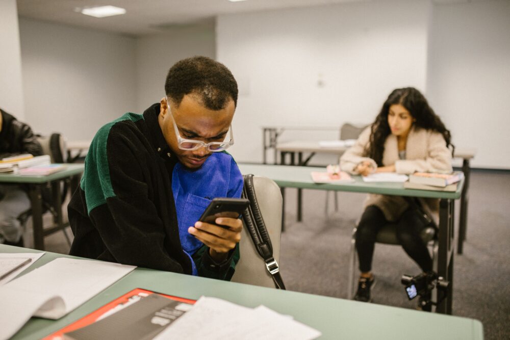 Indian students studying with smartphones and textbooks in a crowded coaching classroom
