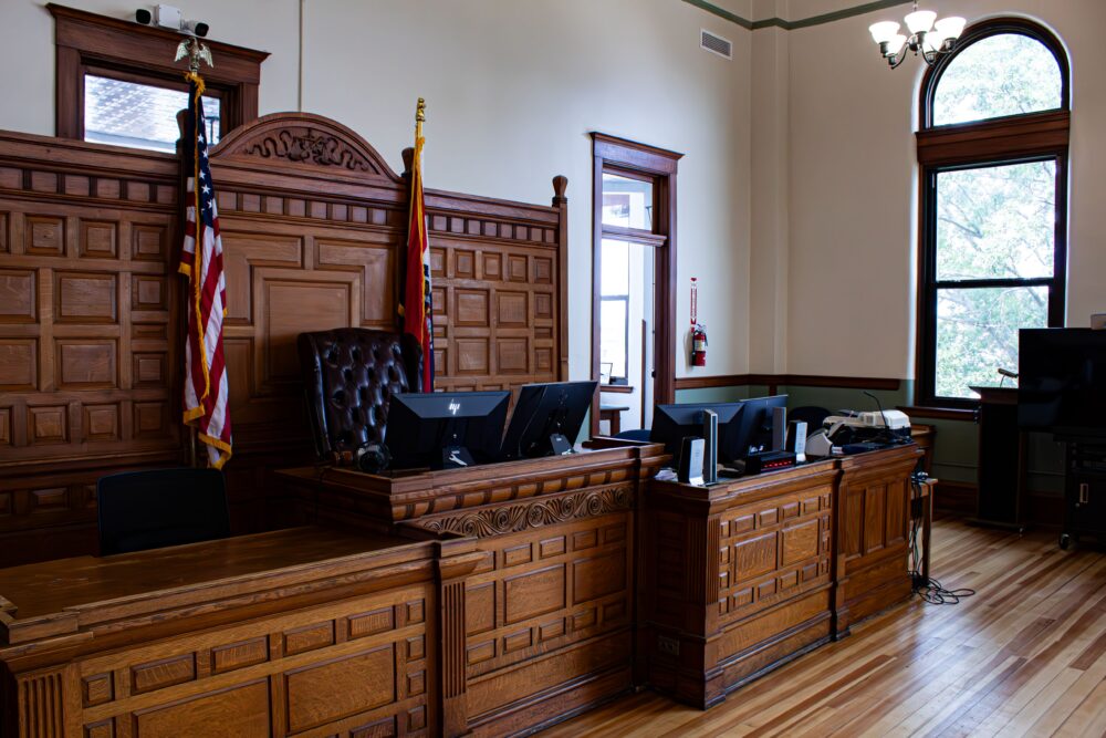 Empty wooden courtroom bench and chairs in an American state courthouse, closed laptop on the desk, soft natural...